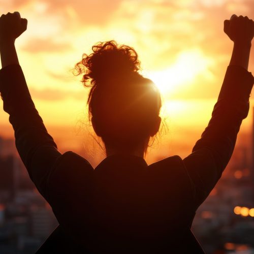 Silhouette of a person celebrating victory with raised arms against a vibrant sunset and city skyline in the background.